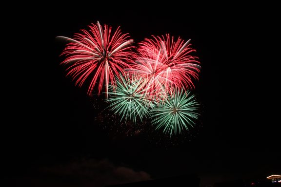 Bunte Feuerwerkskörper in Rot und Grün leuchten vor einem schwarzen Himmel.