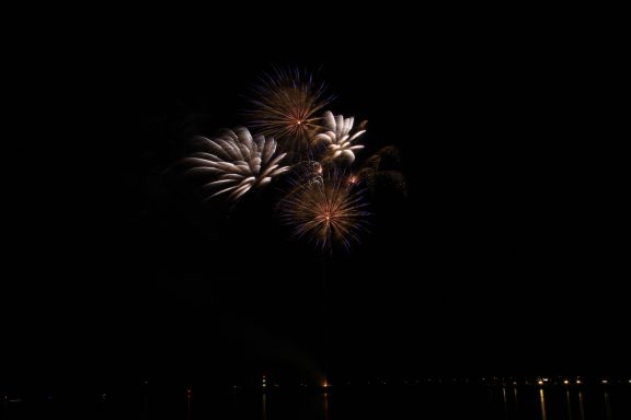 Farbenfrohe Feuerwerke explodieren am Nachthimmel über einem Gewässer.