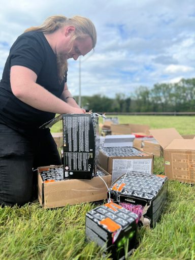 Person mit langen Haaren sortiert elektronische Komponenten auf einer Wiese.