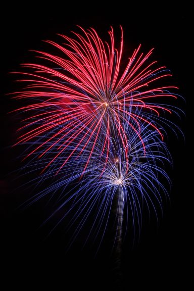 Buntes Feuerwerk mit roten und blauen Effekten vor schwarzem Hintergrund.